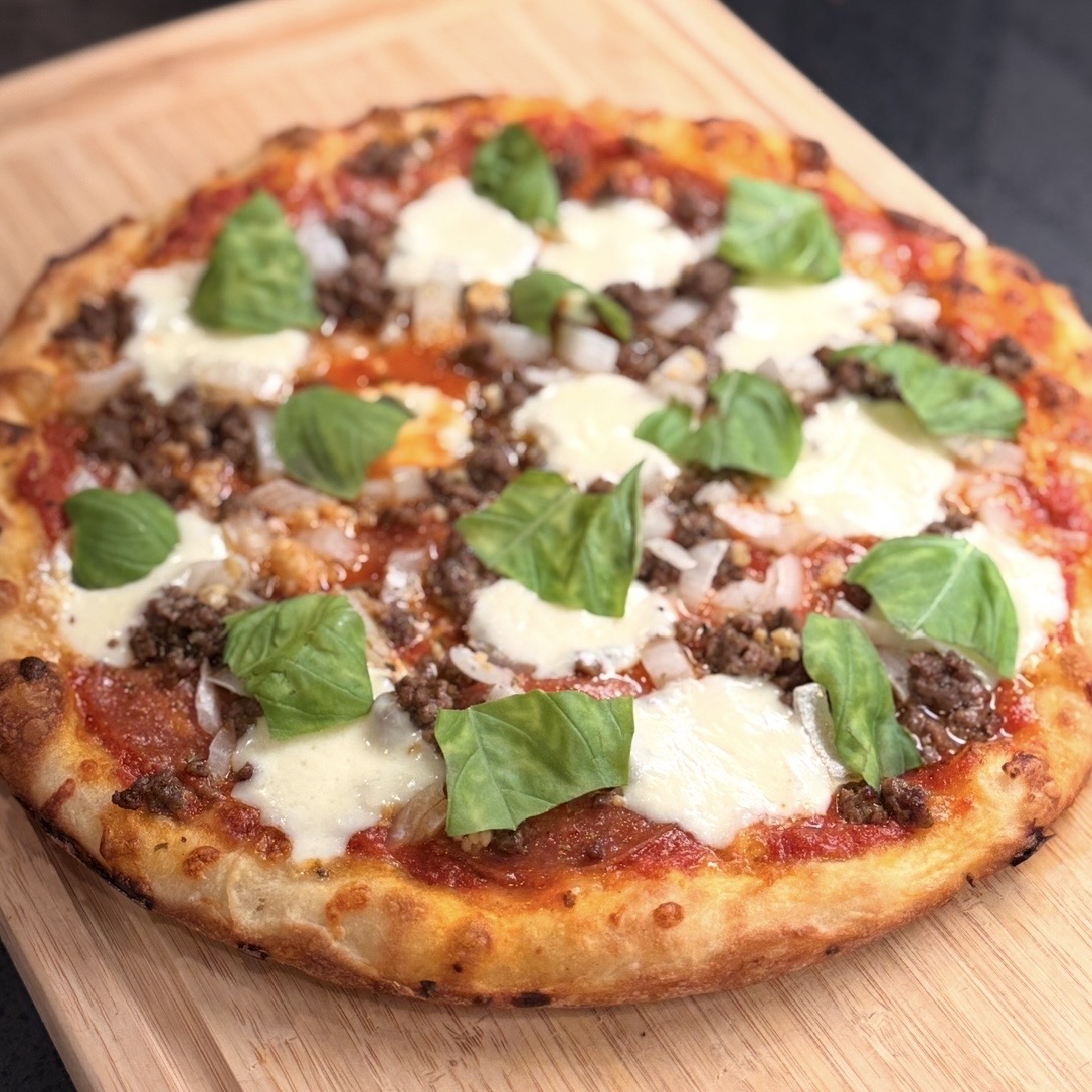 Sausage and basil pizza on a wooden board